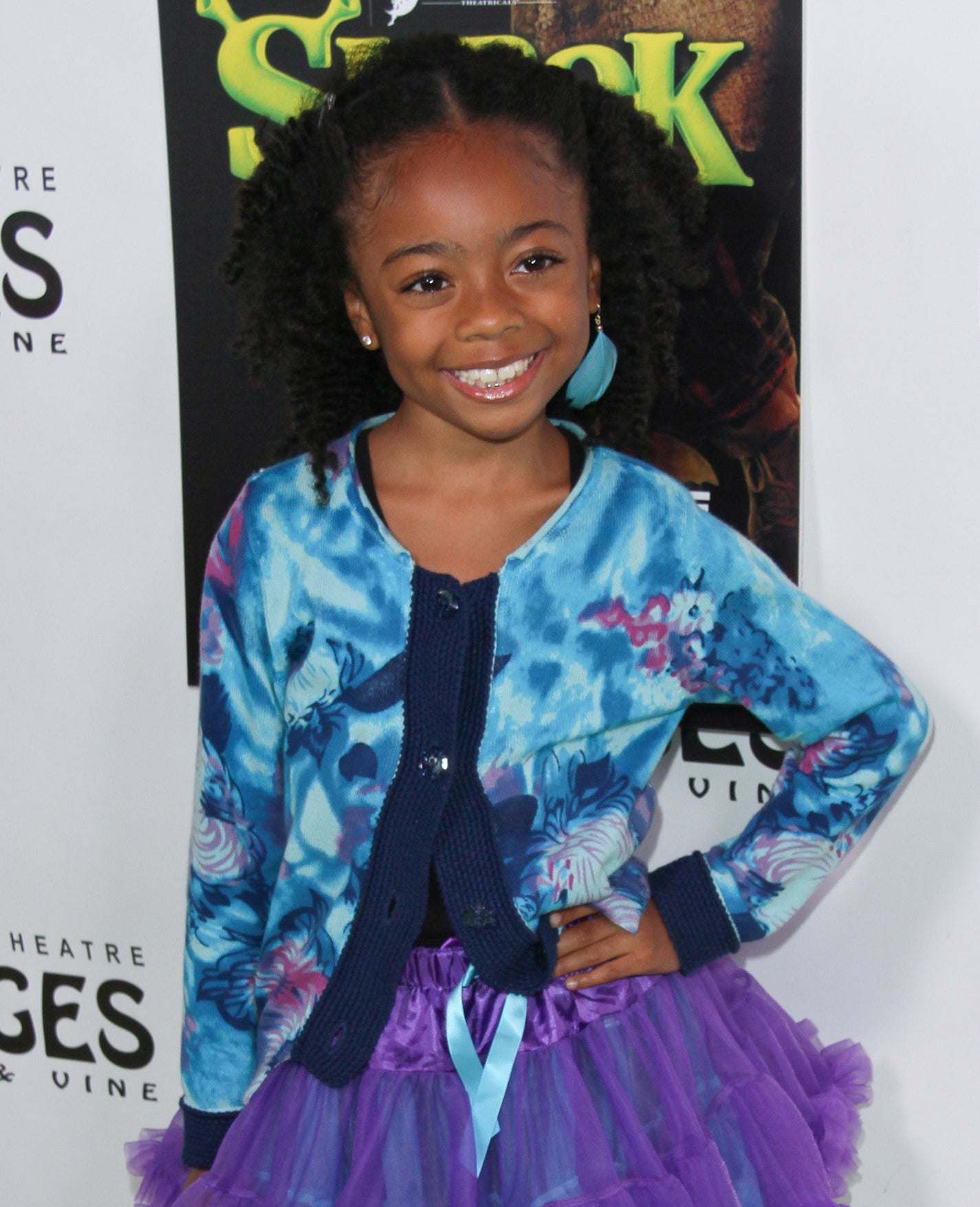 Skai Jackson smiling on the red carpet, wearing a blue cardigan and a purple tutu dress with blue sneakers at the Pantages Theatre Hollywood