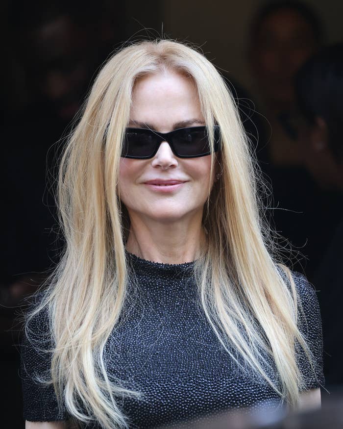 Nicole Kidman smiles while wearing sunglasses and a chic, textured short sleeve top
