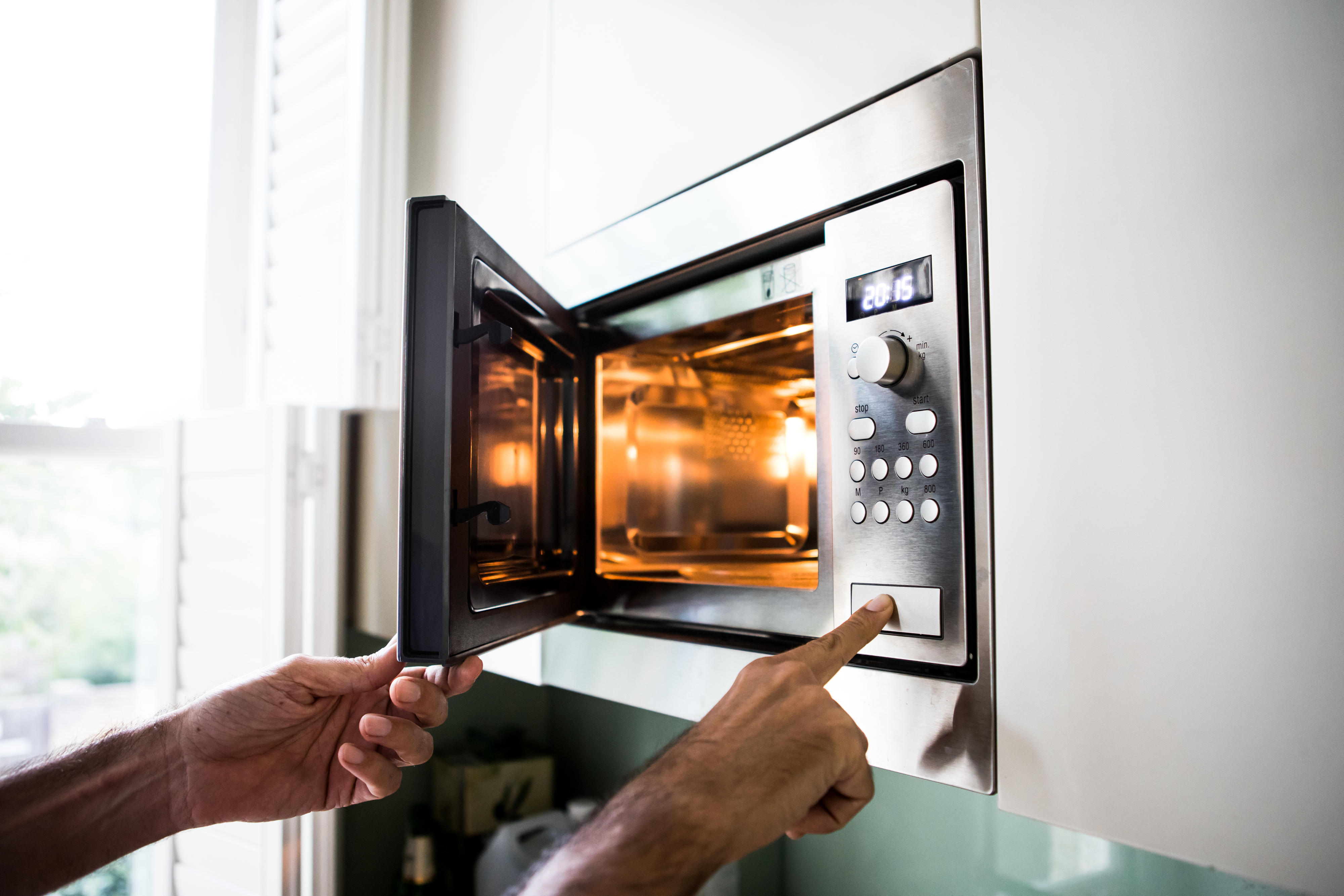 A person is using a microwave, pressing a button while the door is open. The microwave's interior light is on