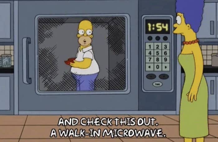 Homer Simpson stands inside a large microwave holding food while Marge Simpson watches. Text, And check this out. A walk-in microwave