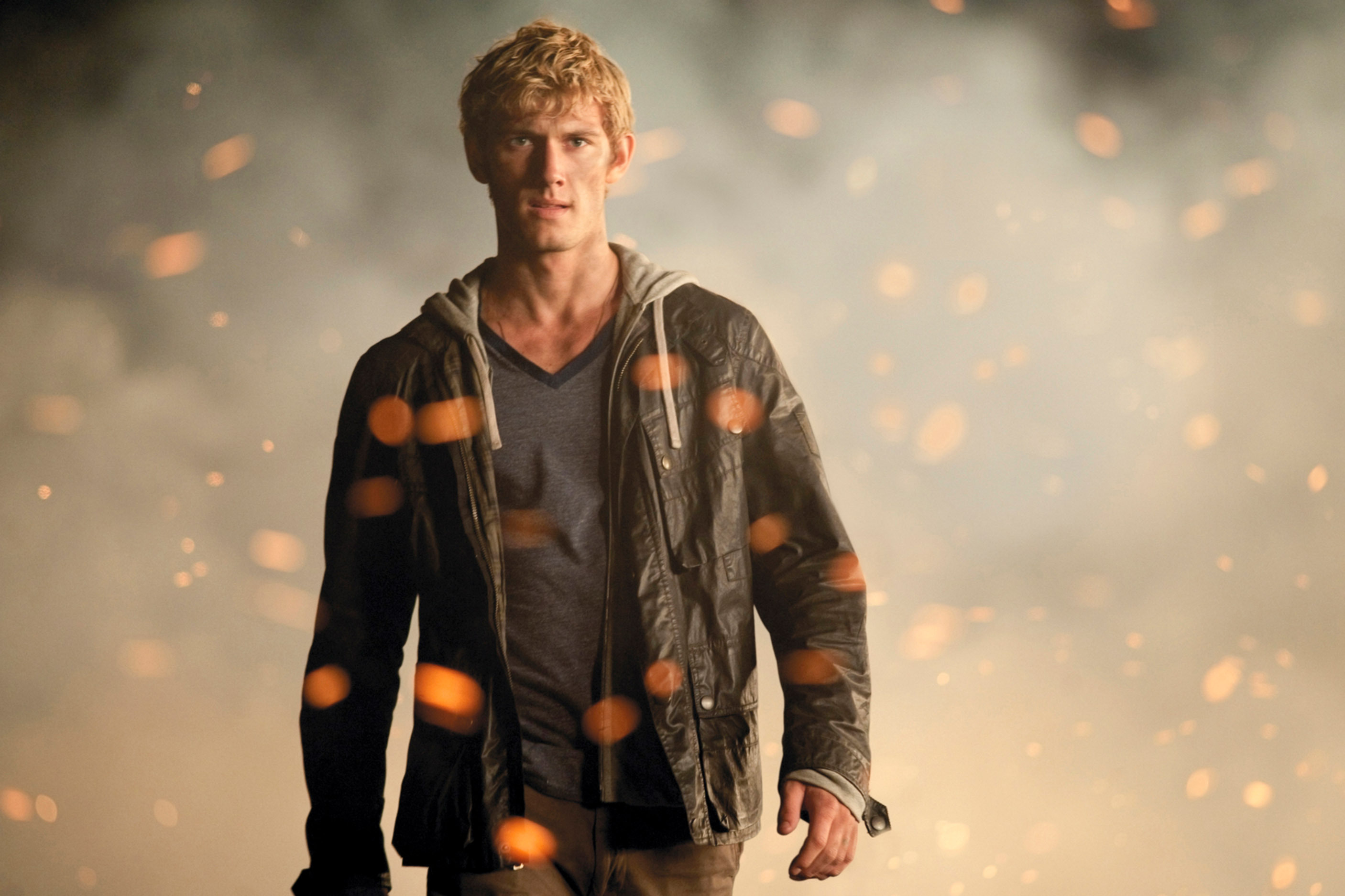 Alex Pettyfer stands in front of a smoky background with embers floating around, wearing a casual jacket over a hoodie and a T-shirt in a scene from &quot;I Am Number Four&quot;