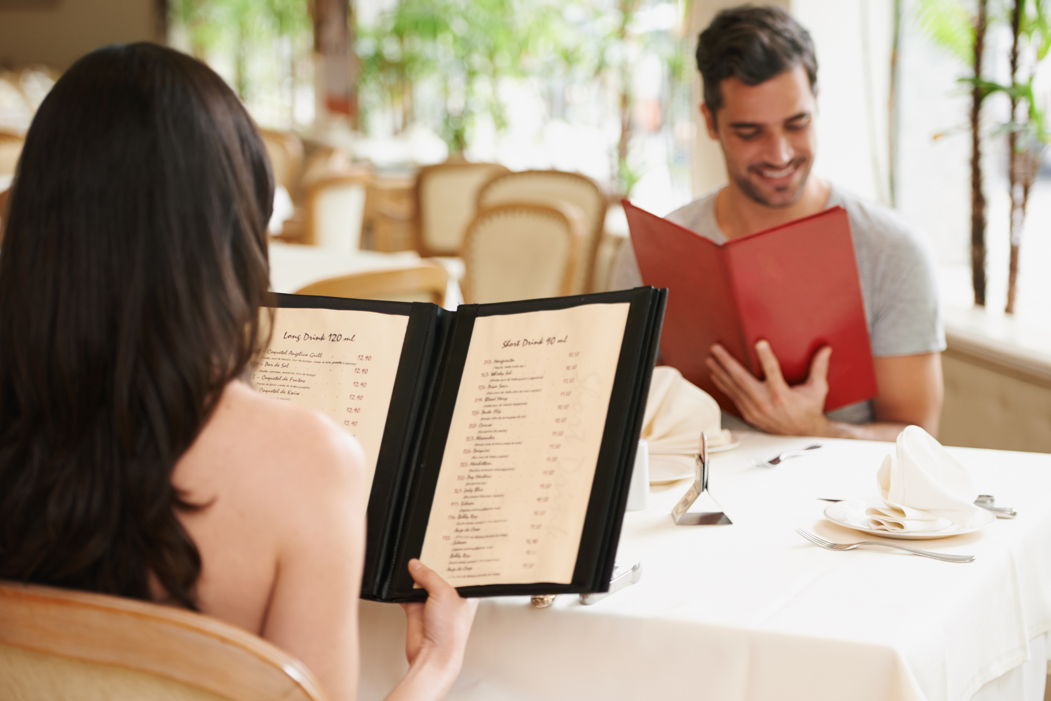 Two people sitting at a table in a restaurant reading menus; one has long dark hair and the other has short dark hair and a beard