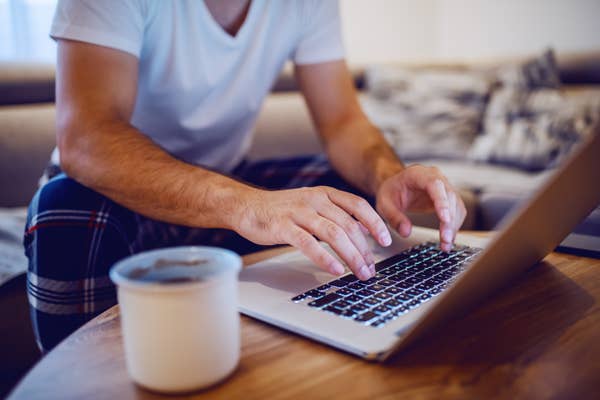 A person in casual clothes types on a laptop at a table with a candle in the foreground