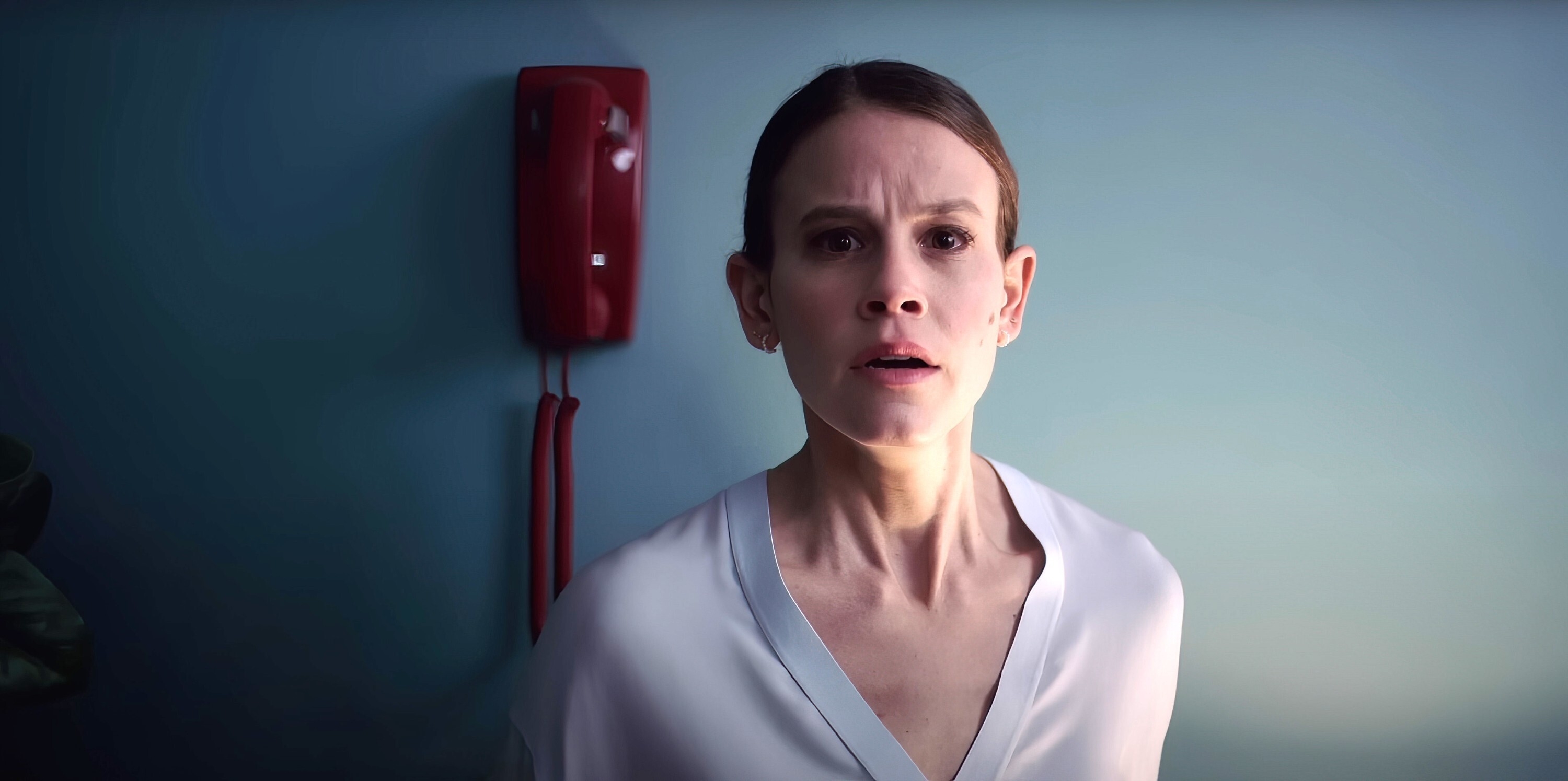 Sosie Bacon with a concerned expression and a red phone in the background in a scene from &quot;Smile&quot;
