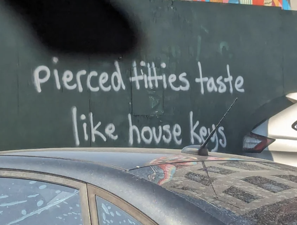 Graffiti on a wall reads, "pierced titties taste like house keys."