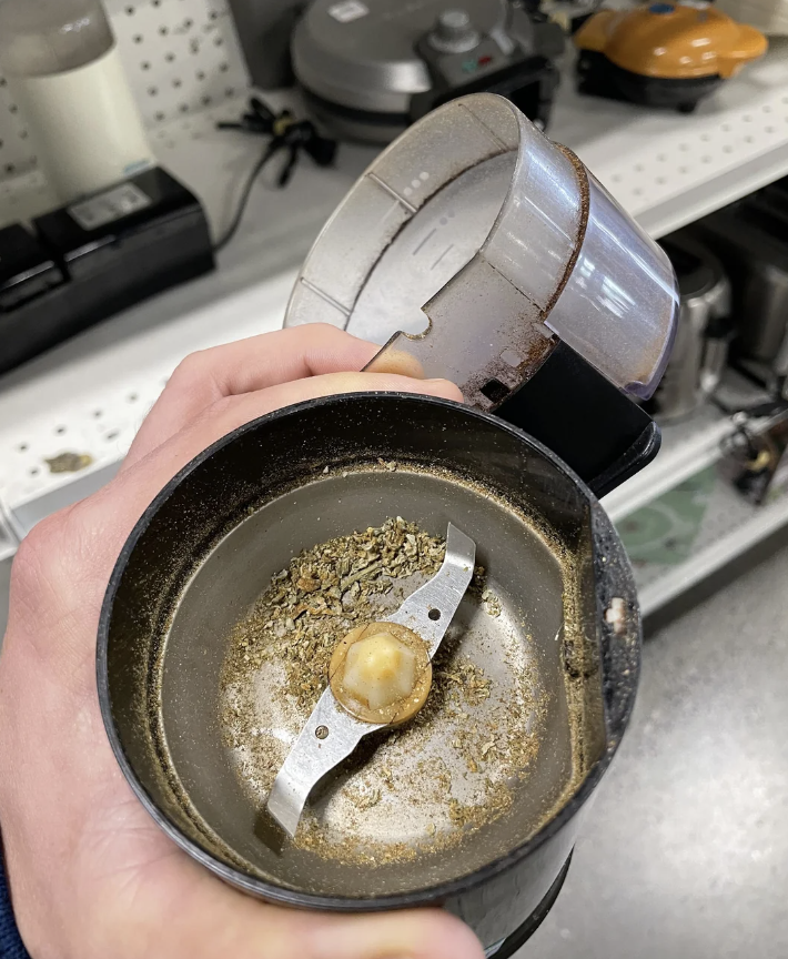 A hand holding a used coffee grinder, showing the residue and remnants of ground coffee and possibly herbs inside the grinder