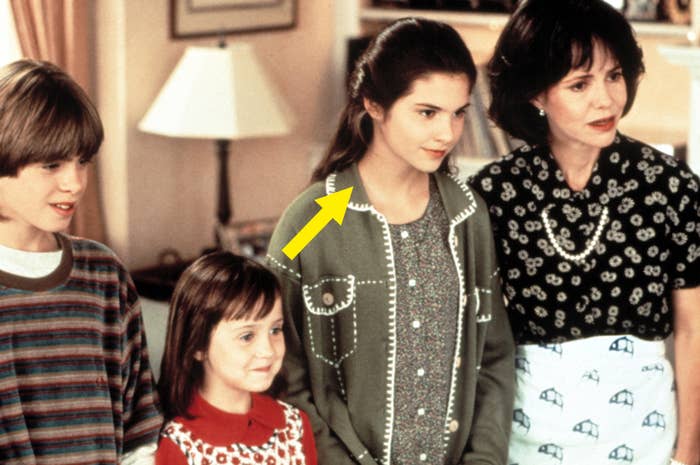 Mara Wilson, Lisa Jakub, Sally Field, and Matthew Lawrence in a living room scene from the movie "Mrs. Doubtfire". A yellow arrow points at Lisa Jakub