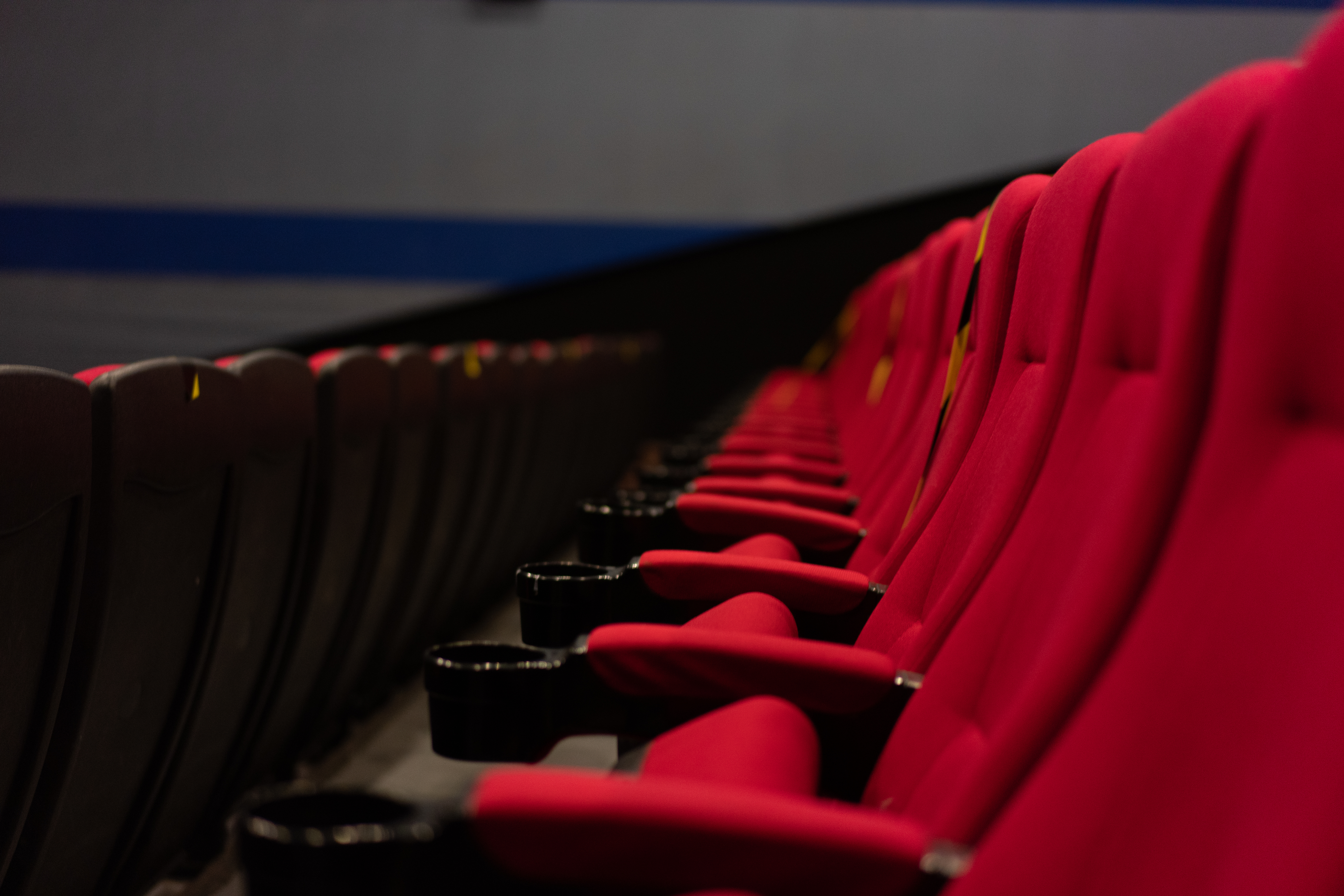 Empty row of theater seats with black armrests in a dimly lit auditorium
