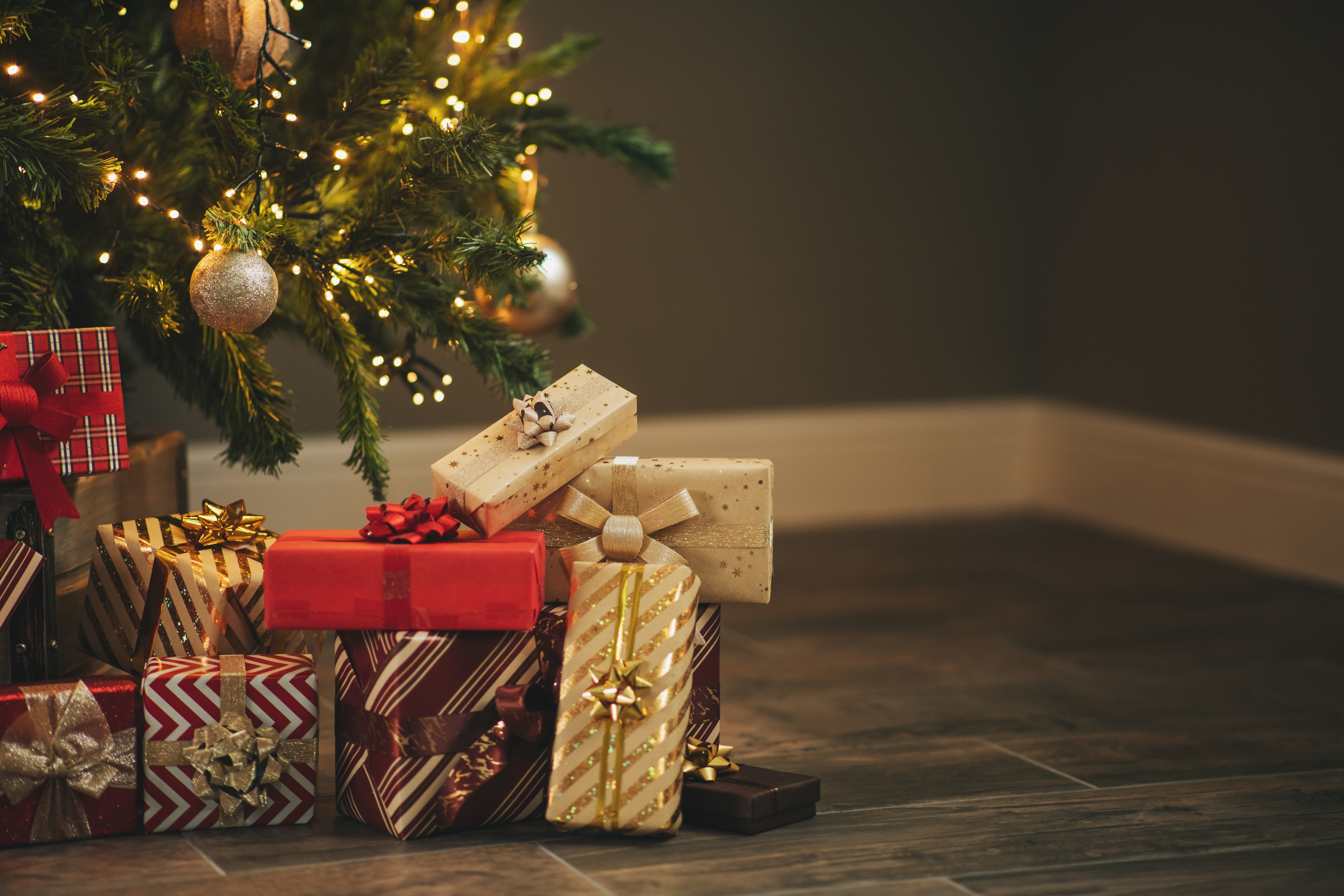 Christmas tree with ornaments and lights, surrounded by multiple wrapped gifts in festive paper and bows