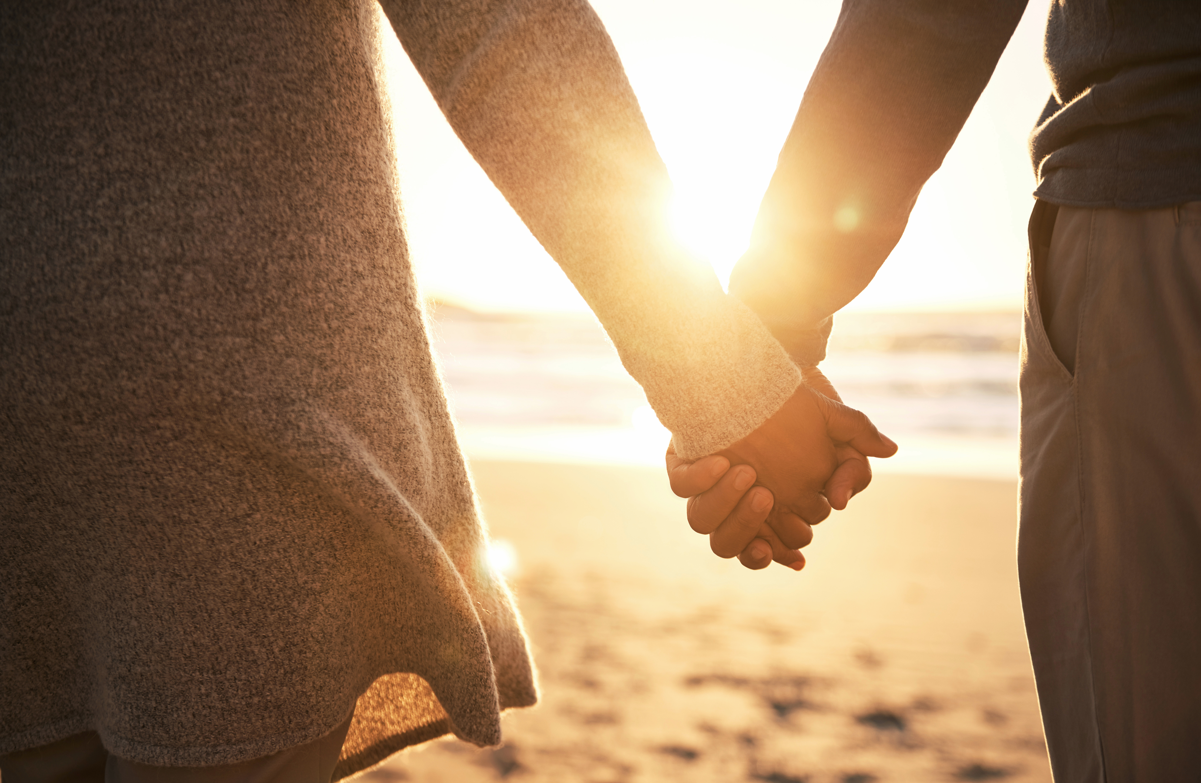 Two people holding hands on a beach at sunset, their faces out of the frame