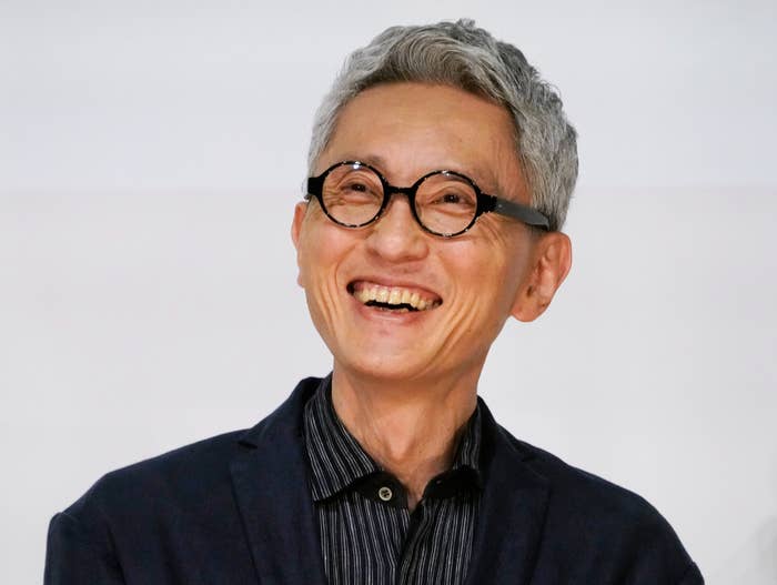 男性が笑顔でカメラを見ています。彼はメガネをかけ、ジャケットとシャツを着用しています。