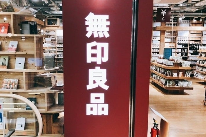 無印良品の店舗内の様子。壁に無印良品と書かれた看板が目立っている。背景に商品棚が見える。