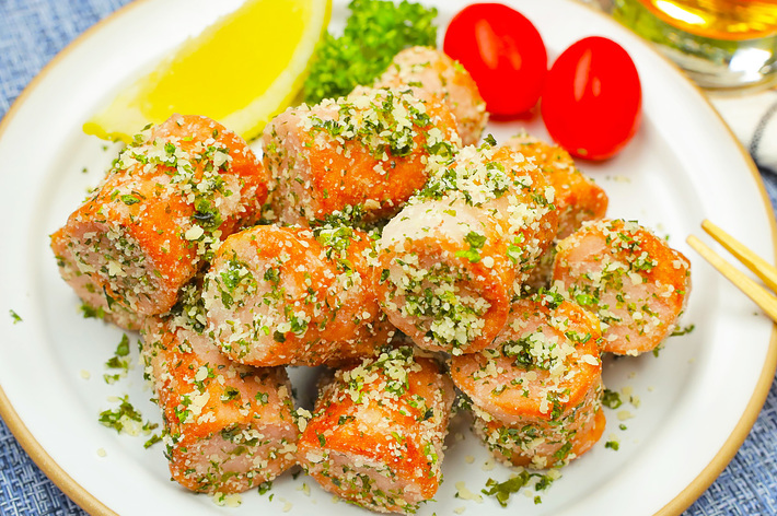 おしゃれな丸皿にハーブとレモンが添えられたパン粉をまぶしたチキンナゲットと、トマトが二つ、ビールの入ったグラスが左上に見える食事のシーン。