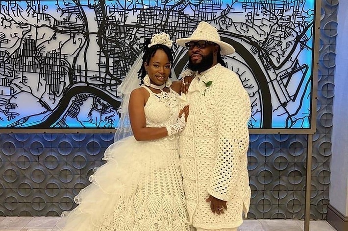 結婚式で新郎新婦が笑顔でポーズを取っています。後ろには都市の地図が描かれたアート作品があります。