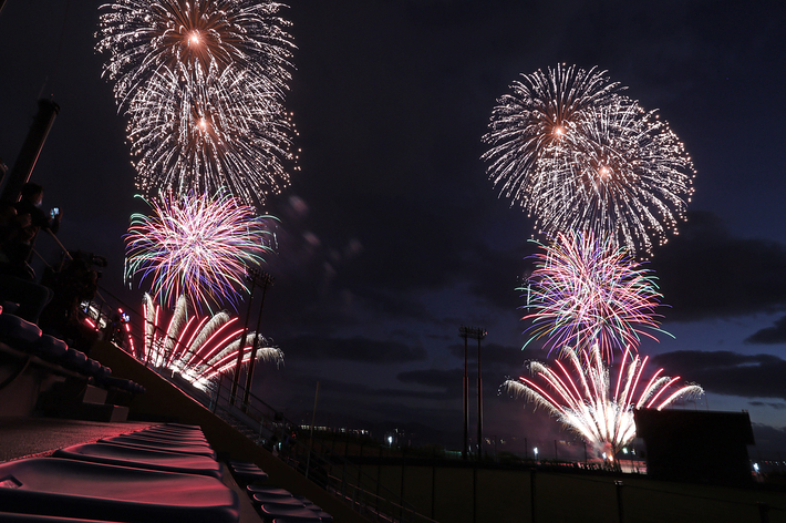 夜空に打ち上げられた壮大な花火が輝いている様子。観客席の屋根越しに見える。