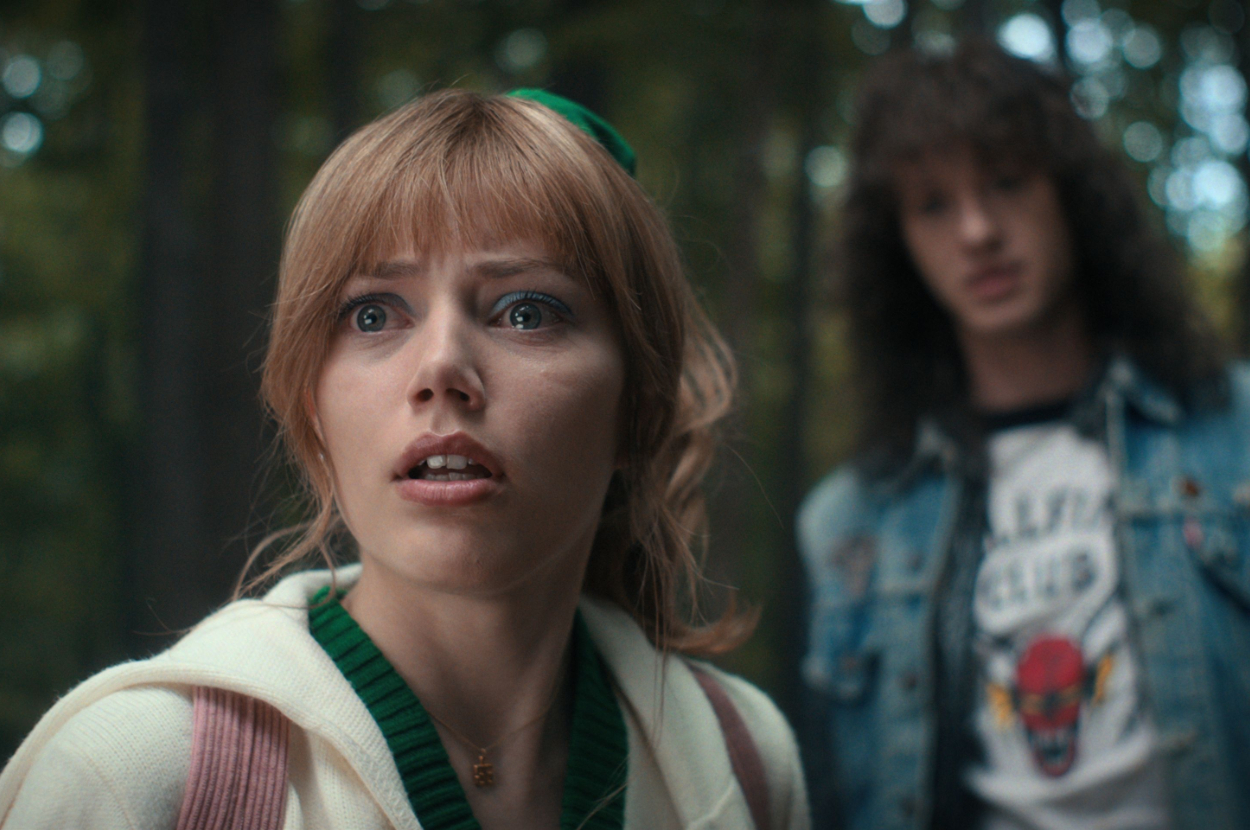 Grace Van Dien and Joseph Quinn in a dramatic scene from a show. Grace looks surprised, with Joseph in the background wearing a denim jacket