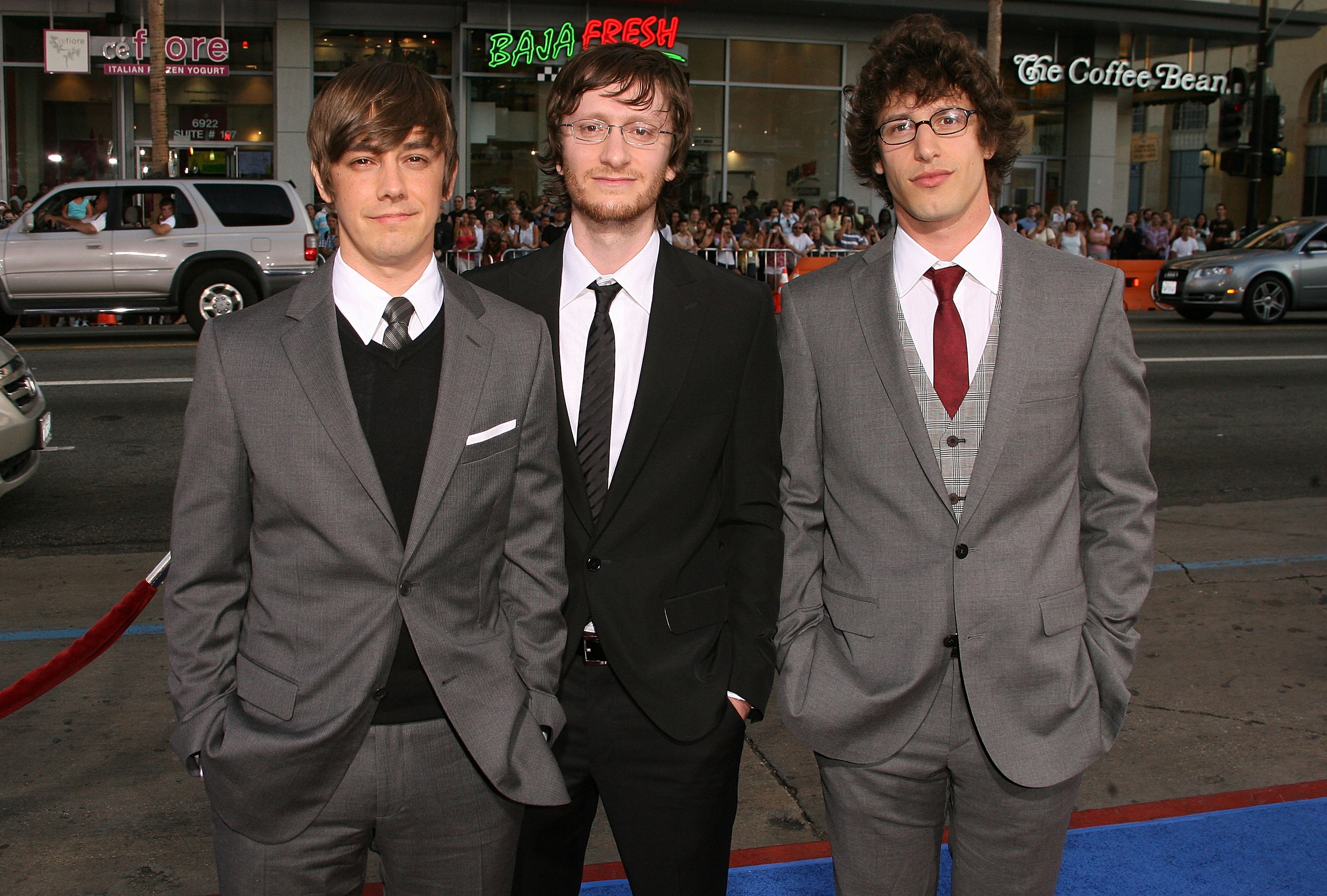 From left to right, Akiva Schaffer, Jorma Taccone, and Andy Samberg stand on a red carpet, all wearing suits
