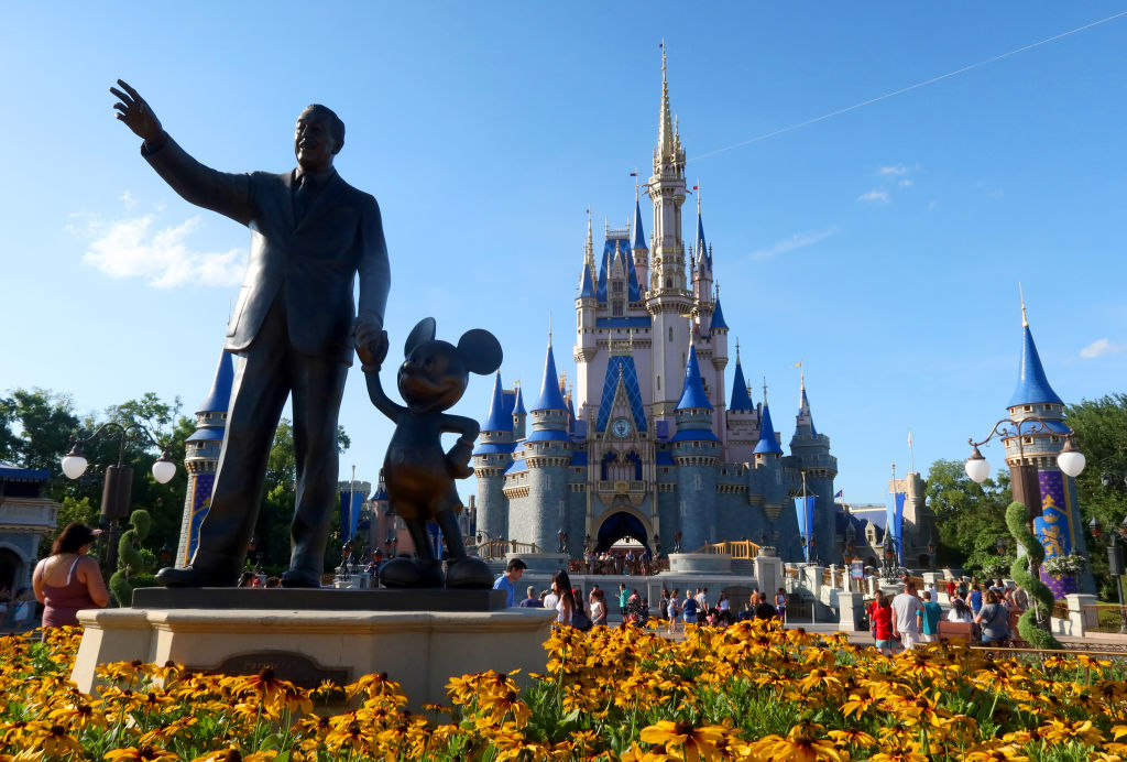 Walt Disney statue holding hands with Mickey Mouse in front of Cinderella's Castle at Disney World, with visitors in the background