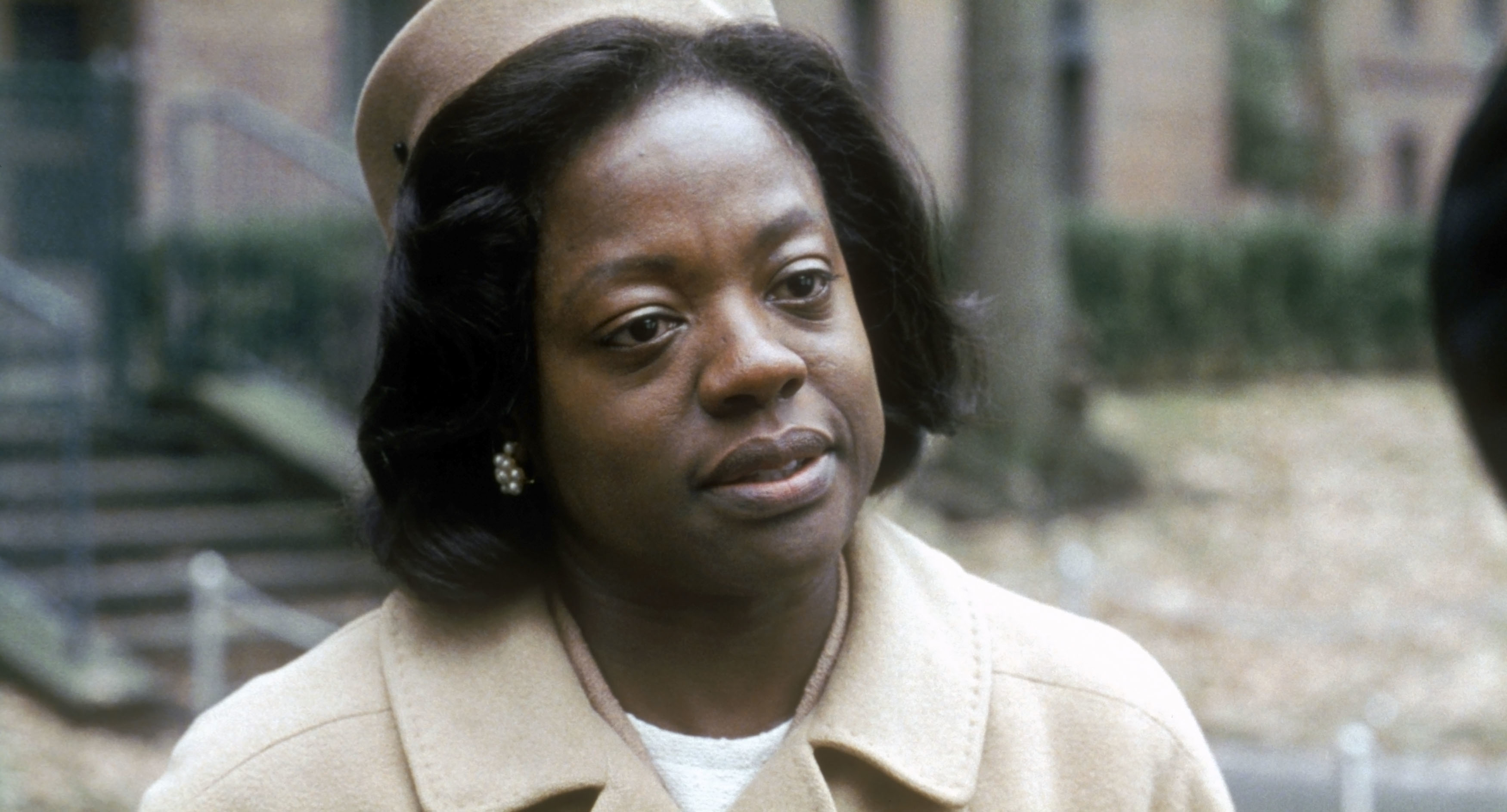 Viola Davis in character, wearing a wool coat and hat, looking serious in an outdoor setting