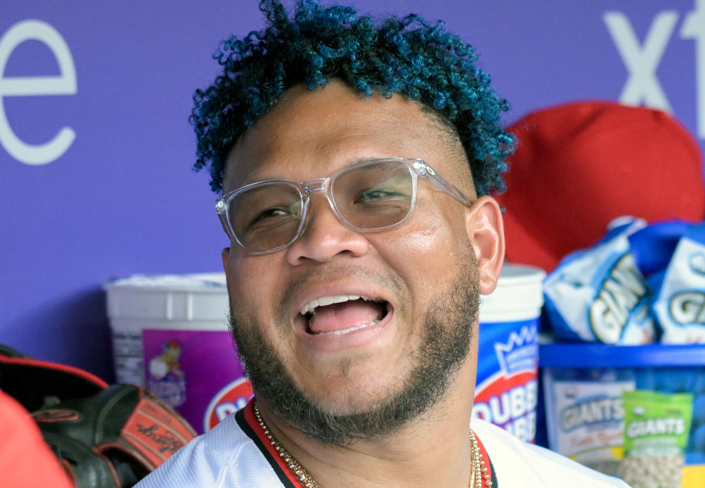 Man wearing glasses smiling in what appears to be a sports team dugout