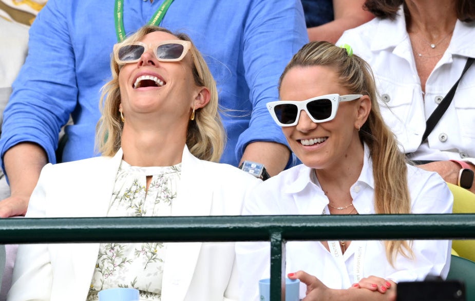 Cameron Diaz and Julie Day at an outdoor event, both wearing sunglasses and white outfits, smiling and laughing