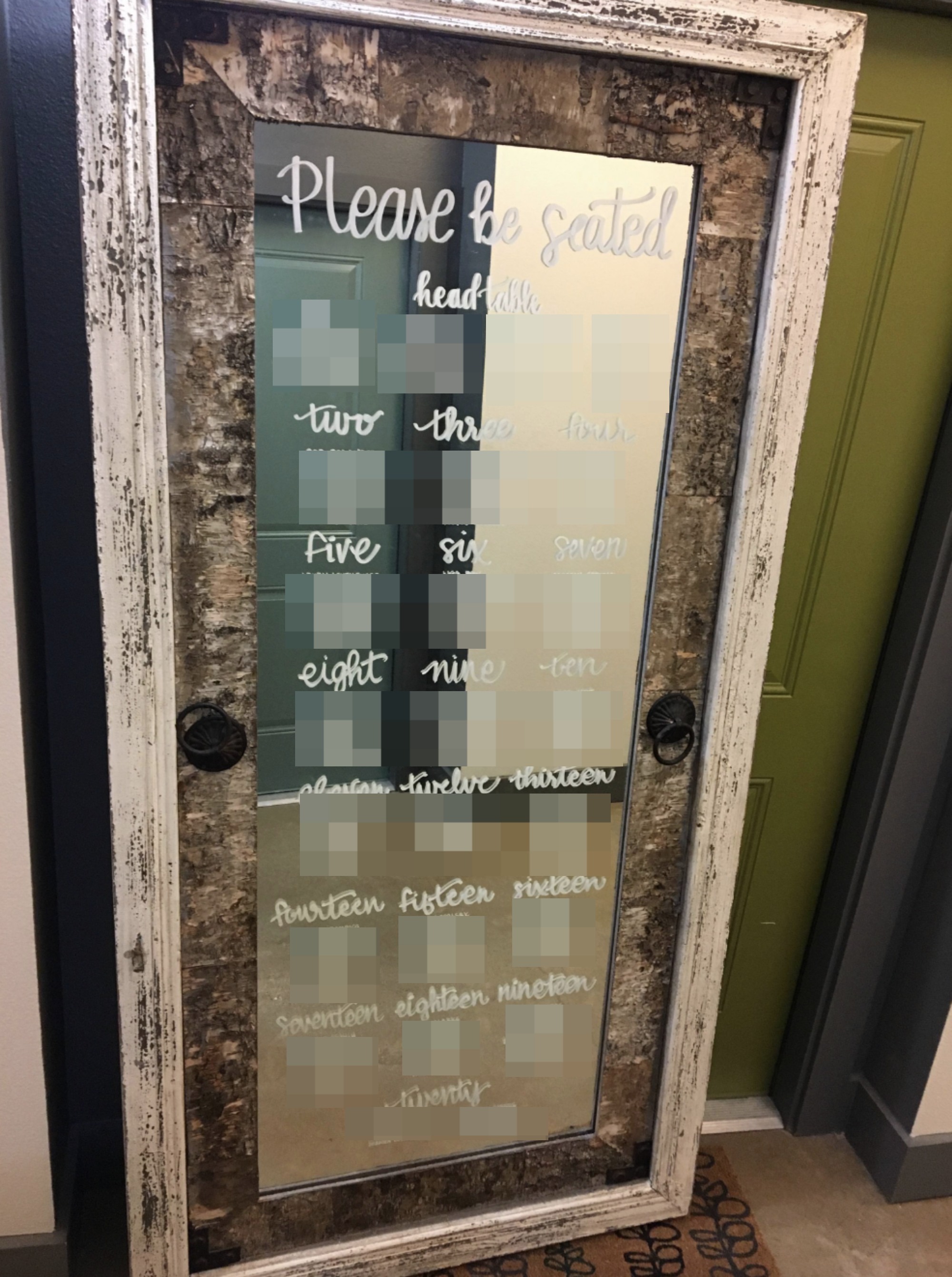 Wedding seating arrangement on a framed glass panel organized by numbered tables from one to twenty; each table lists several guest names