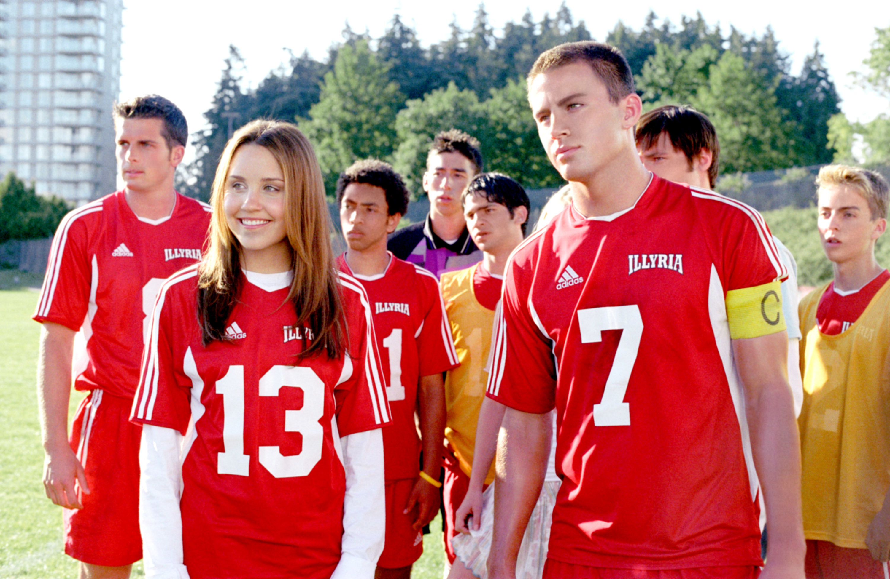 Amanda Bynes and Channing Tatum, in red soccer jerseys numbered 13 and 7, stand with teammates on a soccer field in a scene from "She's the Man."