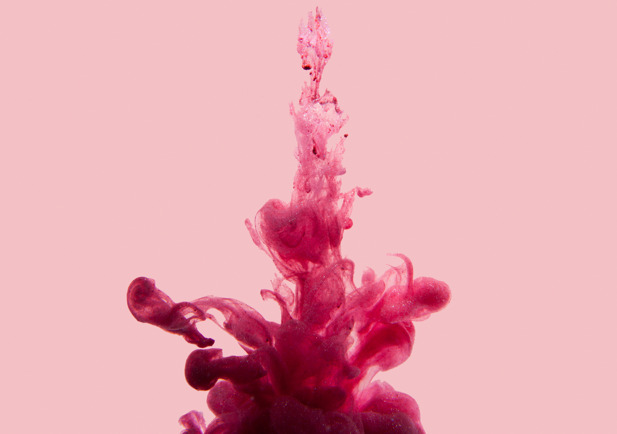 Pink ink swirling in water, creating abstract and intricate shapes against a plain background