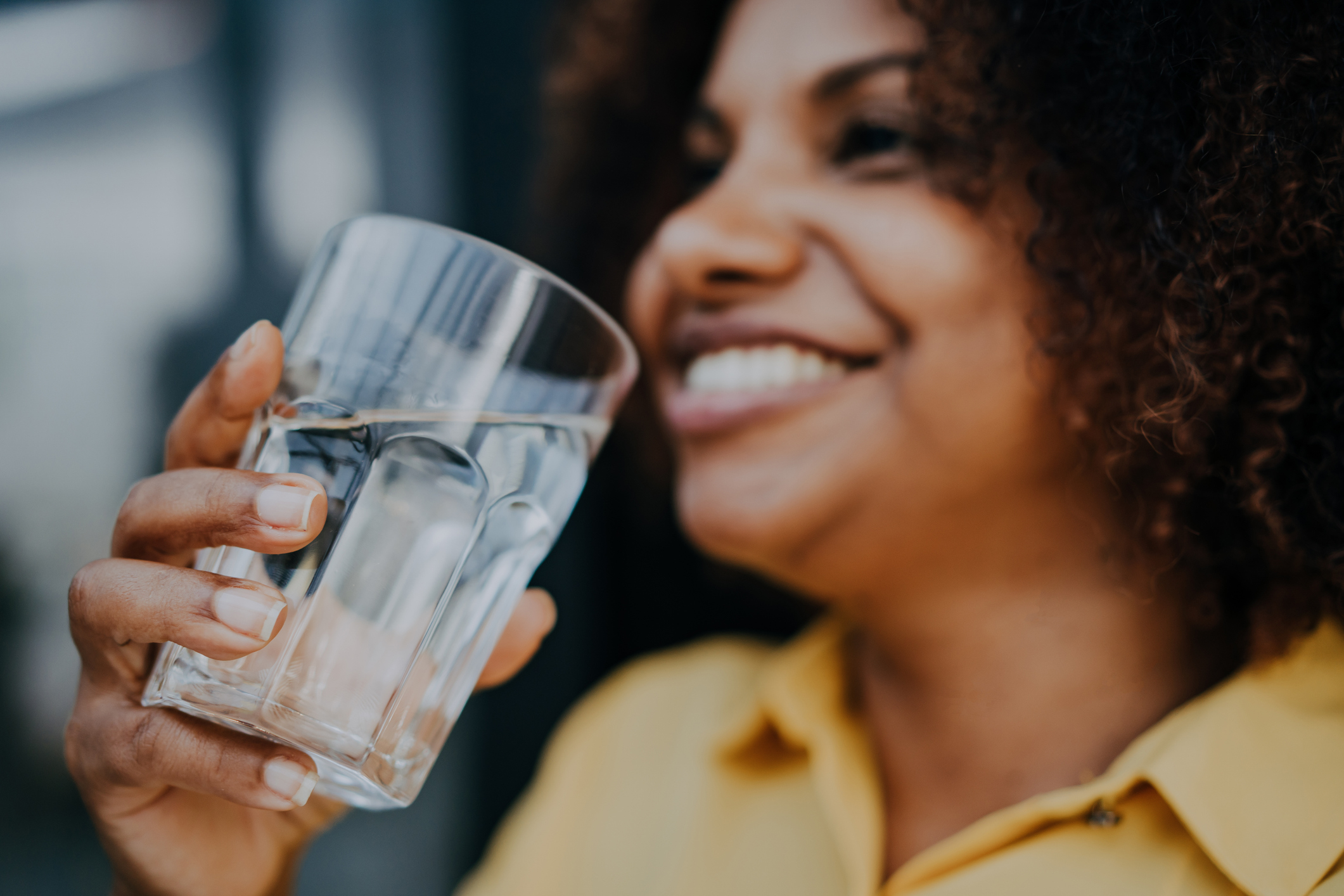 A person is smiling while holding a glass of water close to their face