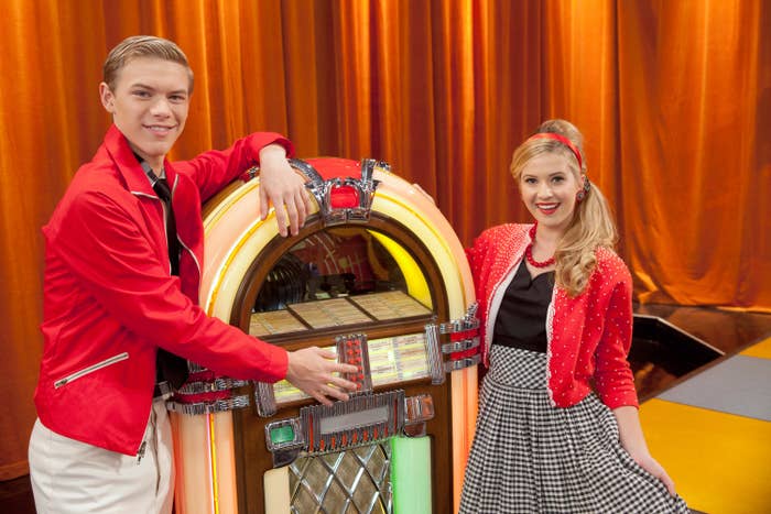 Thomas Brodie-Sangster and Nell Hudson posing by a jukebox. Thomas is wearing a red jacket and white pants, while Nell is in a polka-dot dress with a red sweater