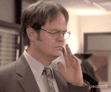 Rainn Wilson as Dwight Schrute from "The Office," wearing a suit and glasses, moves his fingers dramatically around his eyes, mimicking a mentalist
