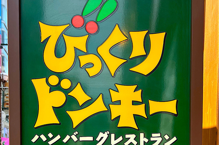 A bright green sign with yellow text that says “Bikkuri Donkey Hamburger Restaurant” in Japanese with an outlet symbol and instructions below