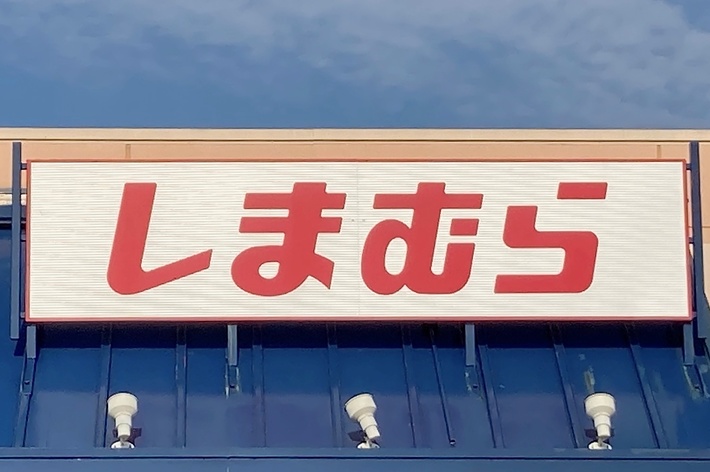 A storefront with Japanese characters on a sign reads &ldquo;Shimamura.&rdquo; The building exterior includes blue awnings and a handicap parking sign