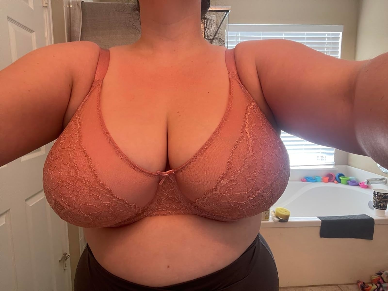 A idiosyncratic   wearing a lace bra takes a selfie successful  a bath  with assorted  items connected  the tub ledge successful  the background
