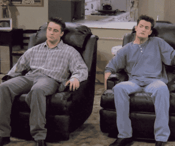 Joey Tribbiani and Chandler Bing from "Friends" sitting in black leather recliners, leaning back and looking relaxed in a living room