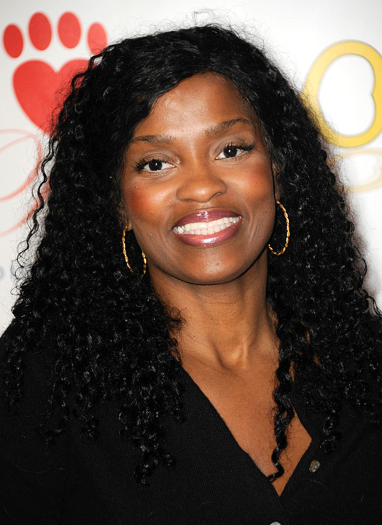 A woman with long curly hair and hoop earrings smiles, wearing a black top