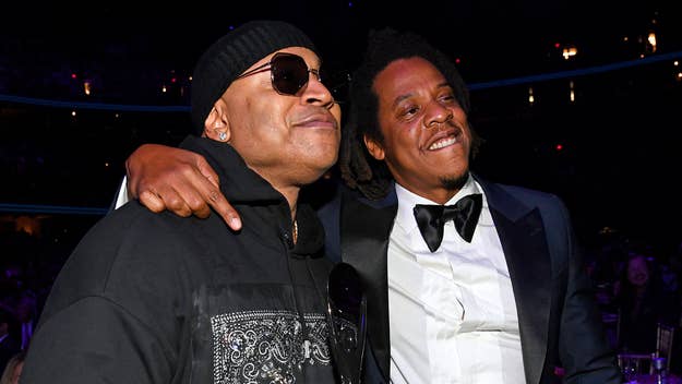 LL Cool J in a black hoodie and beanie, and Jay-Z in a black tuxedo with a bow tie, are smiling and embracing at a music event