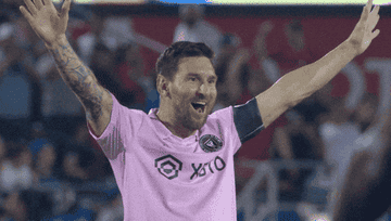 Lionel Messi celebrates on a soccer field with arms raised, wearing a pink jersey from Inter Miami CF