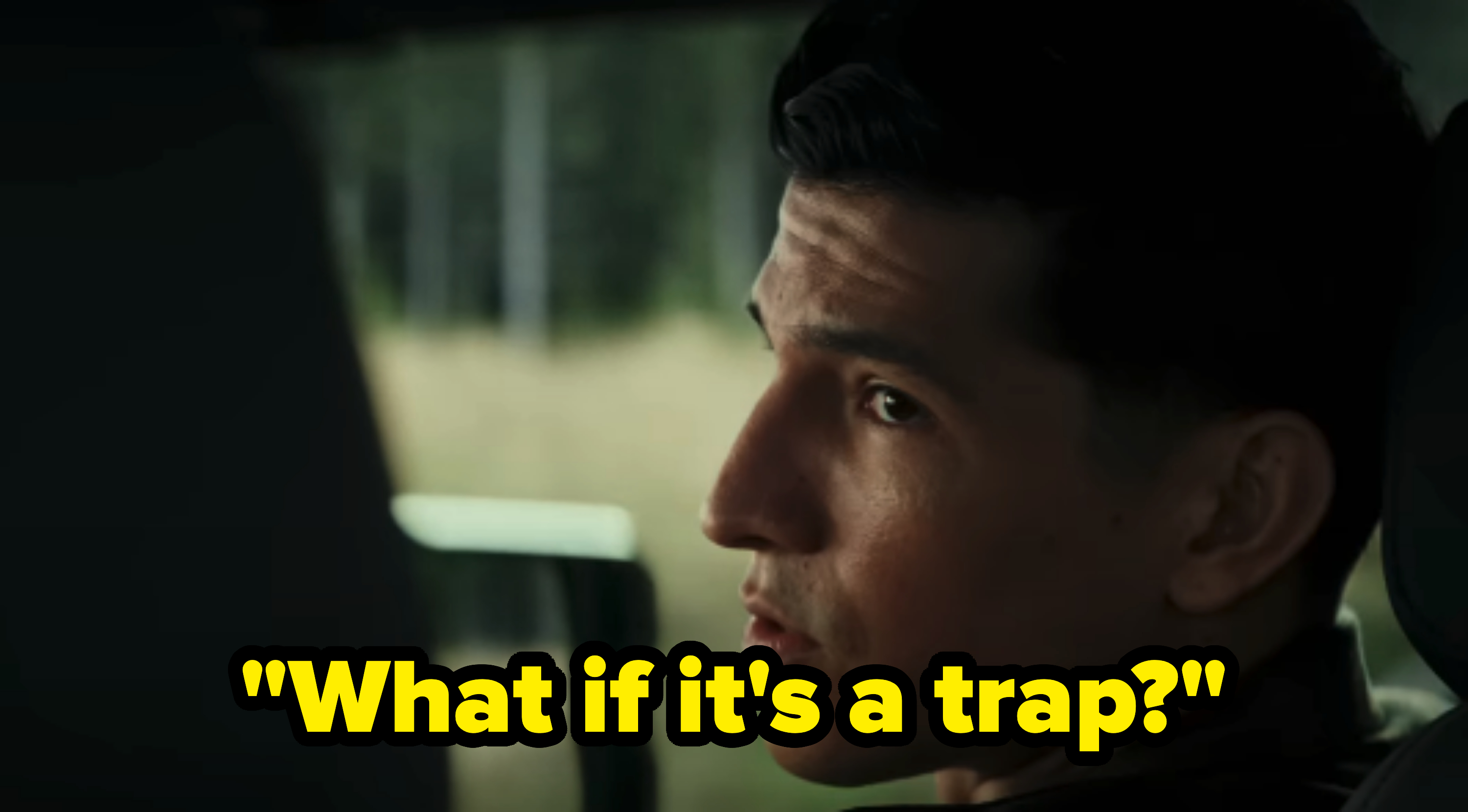 A man sits in a car while looking out the window with a concerned expression