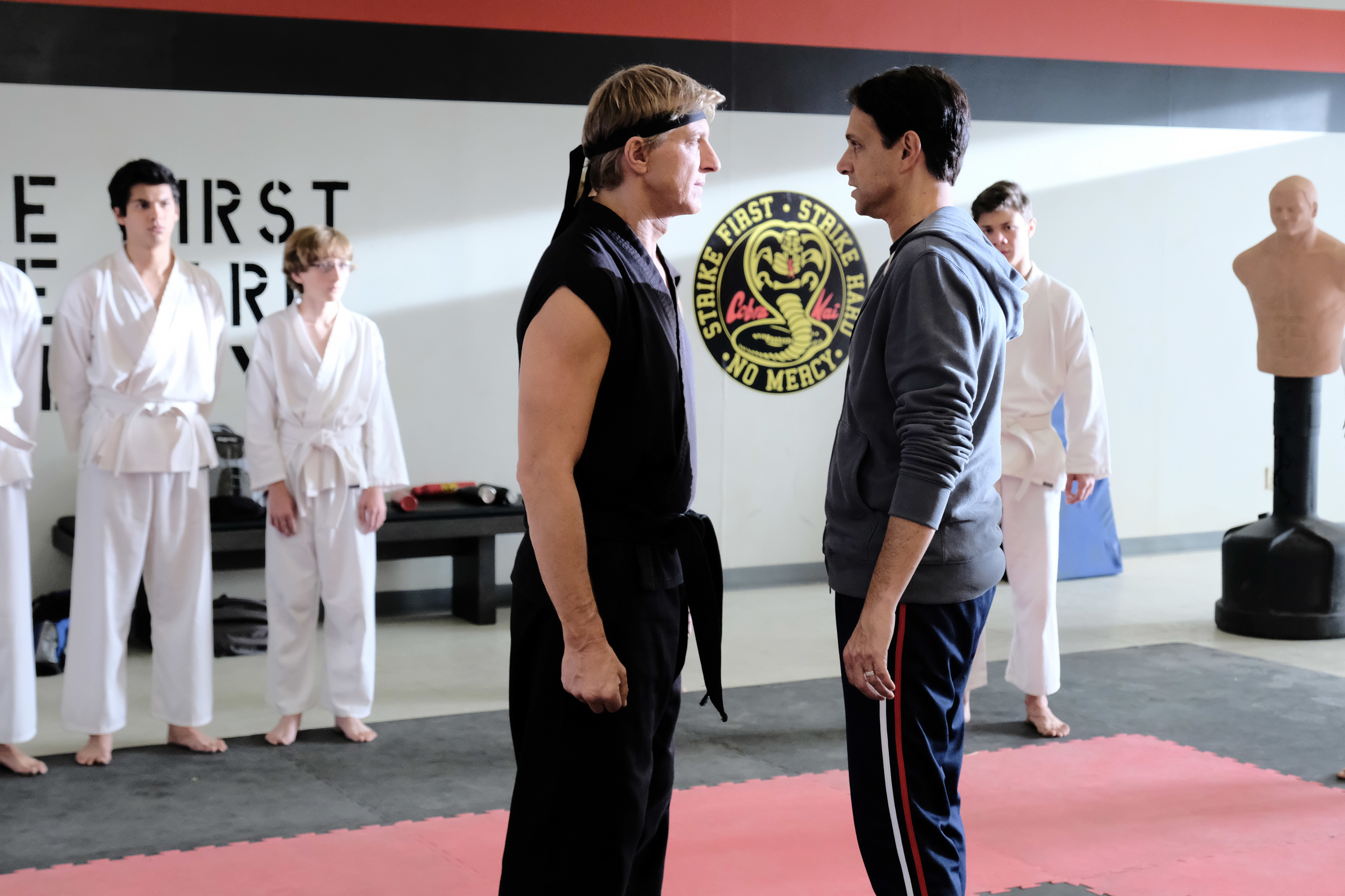 William Zabka and Ralph Macchio facing off with karate students behind them in a scene from &quot;Cobra Kai&quot;
