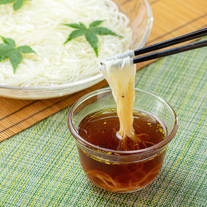 ガラスの器に盛られたそうめんを、つゆに浸けている様子。