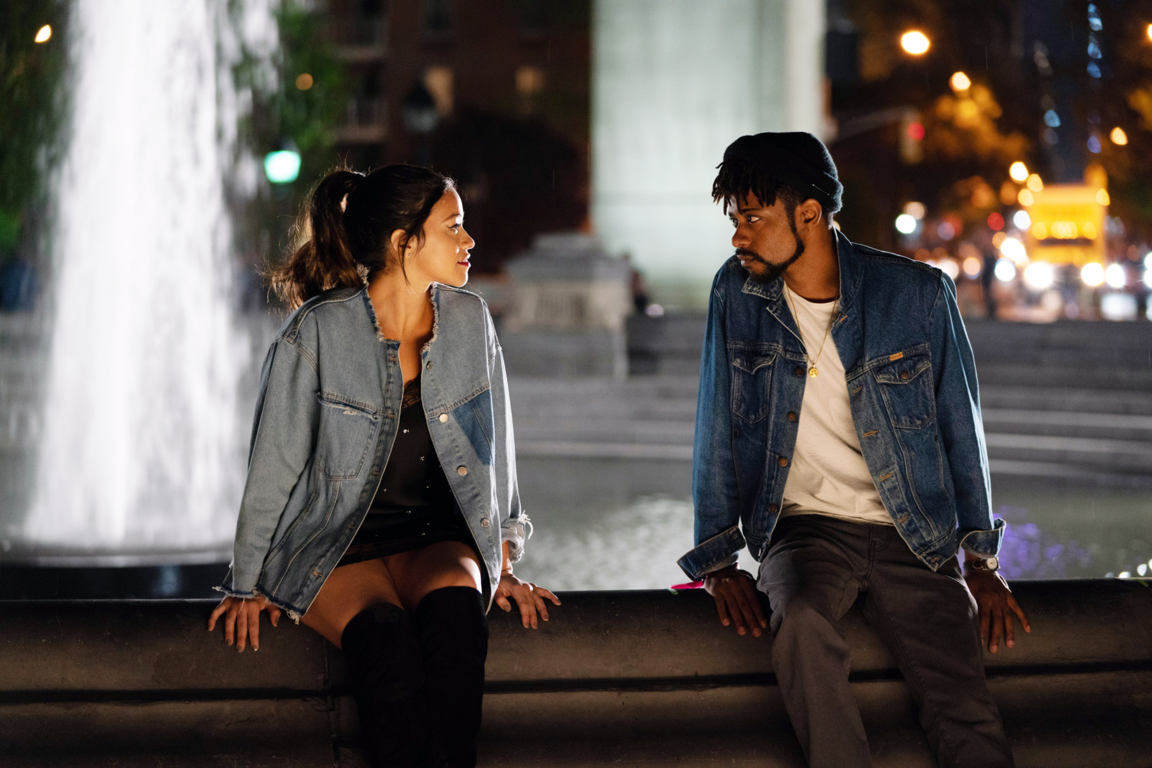 Gina Rodriguez and LaKeith Stanfield sitting in front a fountain in denim jackets in a scene from "Someone Great"