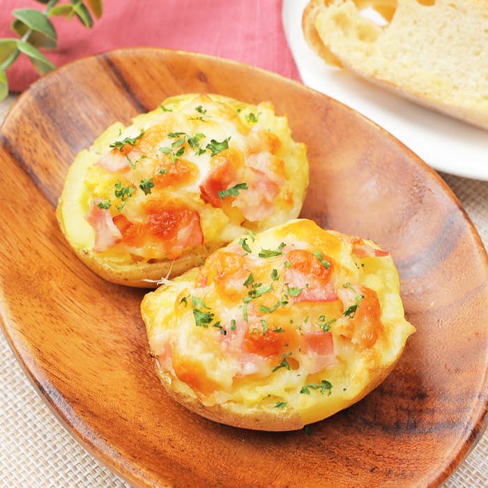 木製の皿にのった、ベーコンとチーズがトッピングされた2つの焼きポテト。