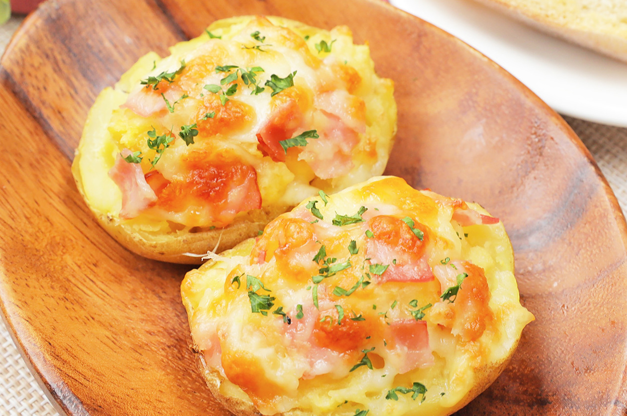 じゃがいものチーズ焼きが木の皿に2つ並んでいます。背景にパンが見えます。