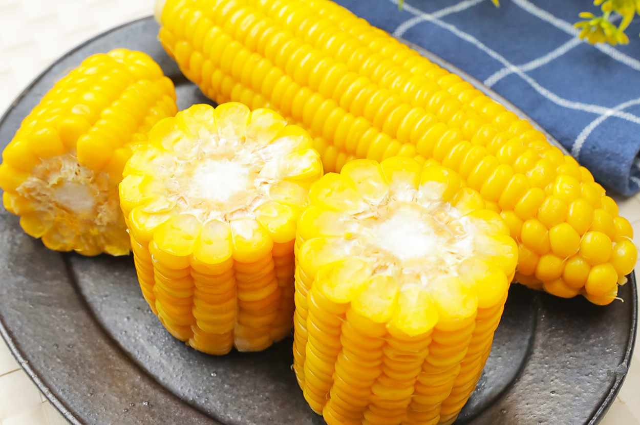 お皿に乗った茹でたとうもろこしの全体と輪切り、花が添えられたテーブルセッティング。