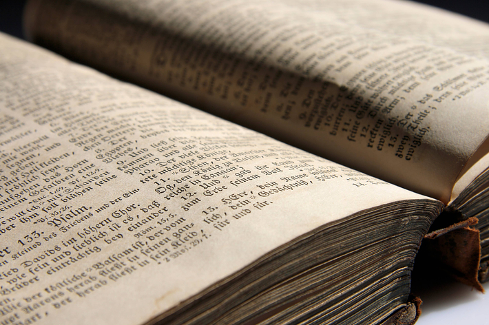 男性が会議室で机に向かい、各種書類や飲み物が置かれている。背景にはアメリカ国旗とオクラホマ州の旗がある。男性の名前は不明。