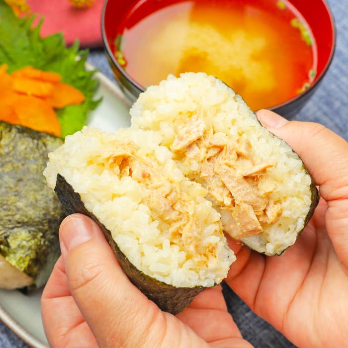 おにぎりが映っています。背景には味噌汁と野菜の添え物も見えます。