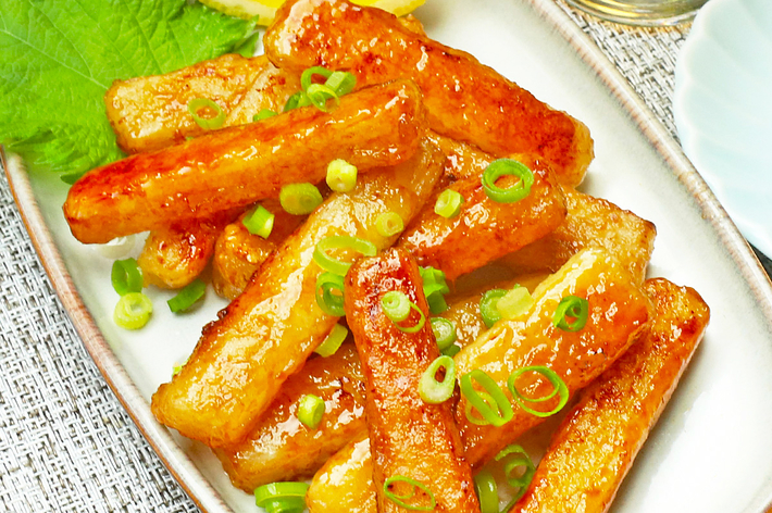 レモンのクォーターとカクテルソースで飾られた角切りの揚げ物。料理の上に刻んだネギがトッピングされている。