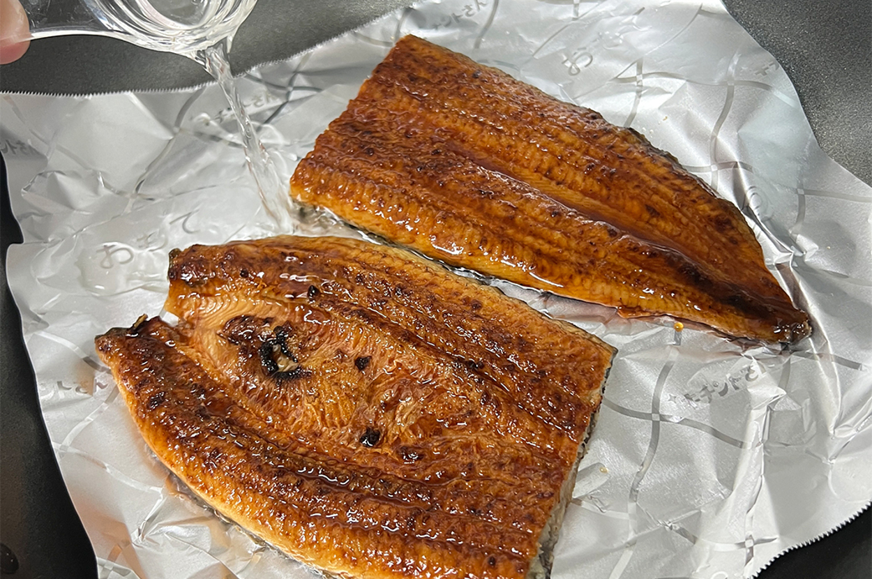 鍋にクッキングシートを敷き、うなぎのかば焼きに液体調味料を注いでいる調理の様子。