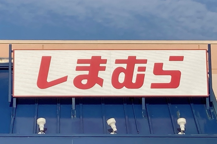 Storefront with a sign in Japanese text above the entrance, which reads “Shimamura.” The foreground shows part of a handicap parking sign